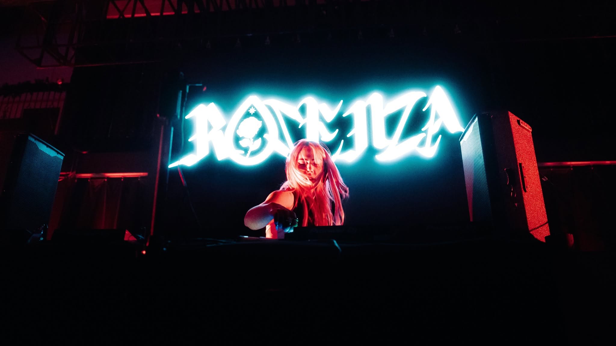 ROZENZA at the decks beneath a glowing ROZENZA logo under red stage light